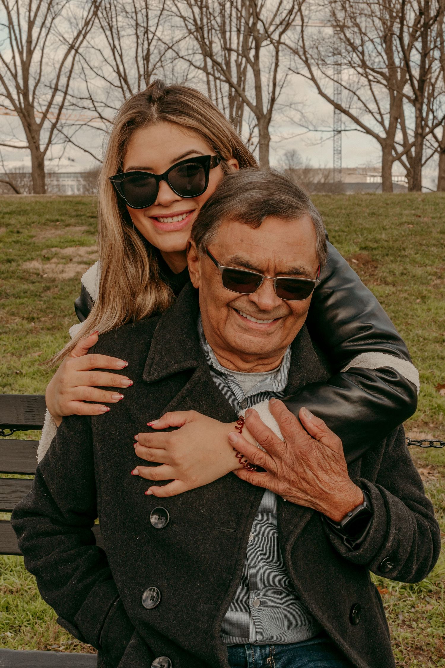 Two people in warm coats sharing a joyful embrace while sitting on a bench outdoors.