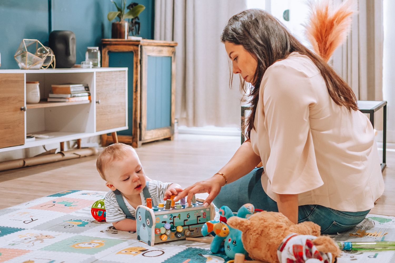 Mother and baby playing with toys on a patterned playmat at home.