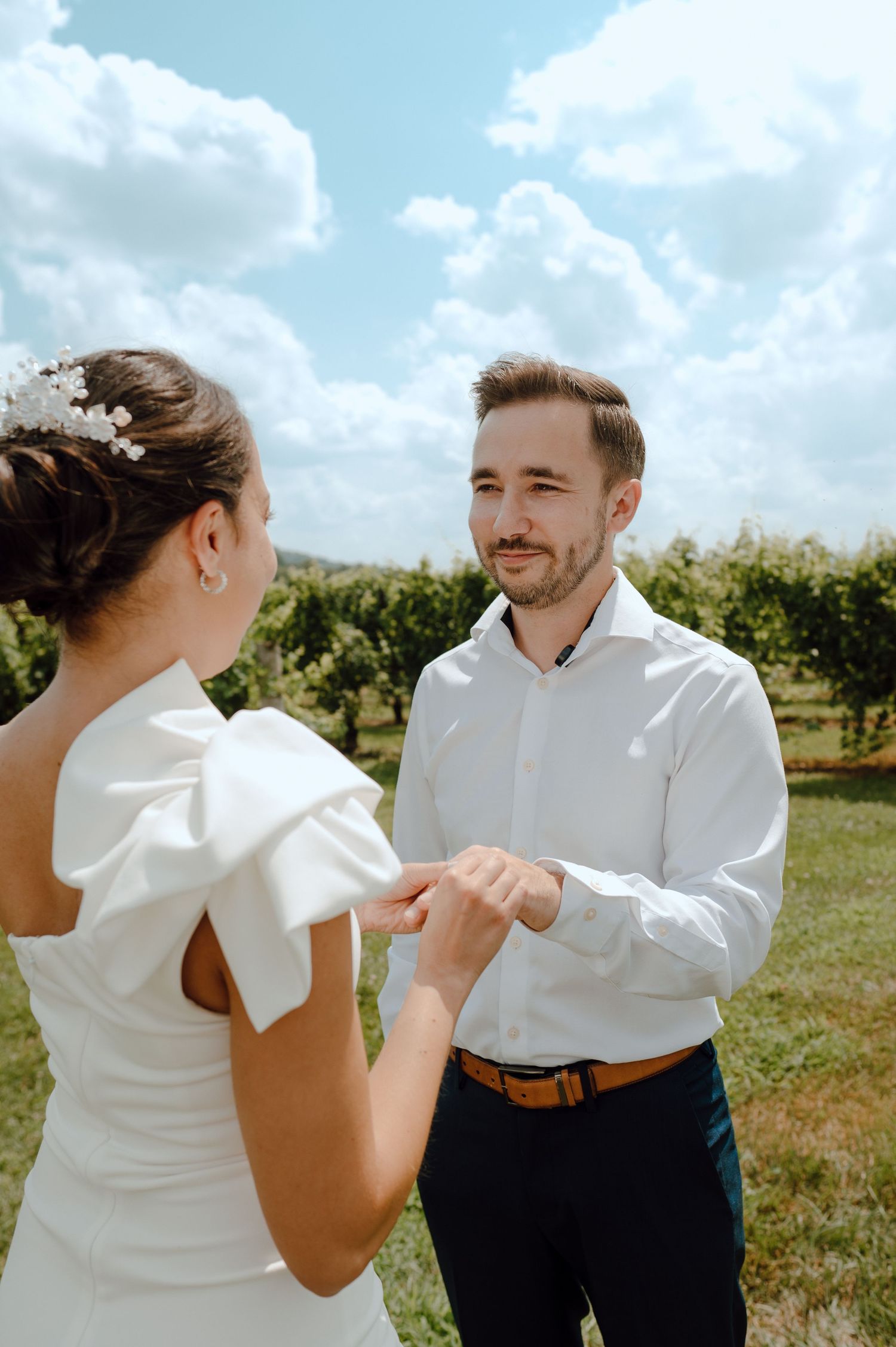 A couple in wedding attire dance together in a sunny outdoor orchard setting, creating a joyful and intimate moment.