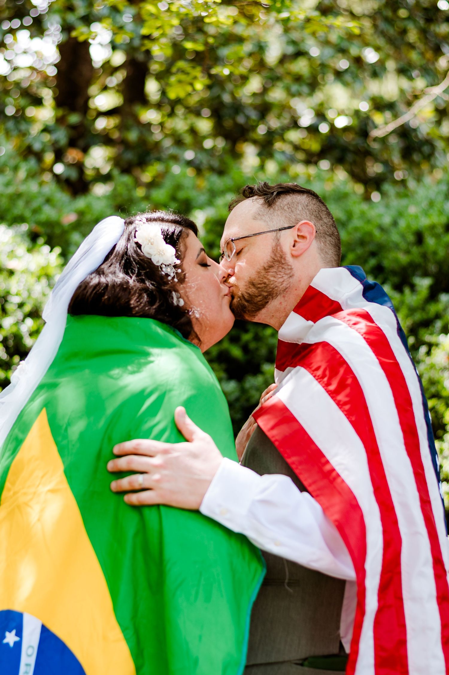 A couple kisses while wrapped in Brazilian and American flags during their wedding celebration.
