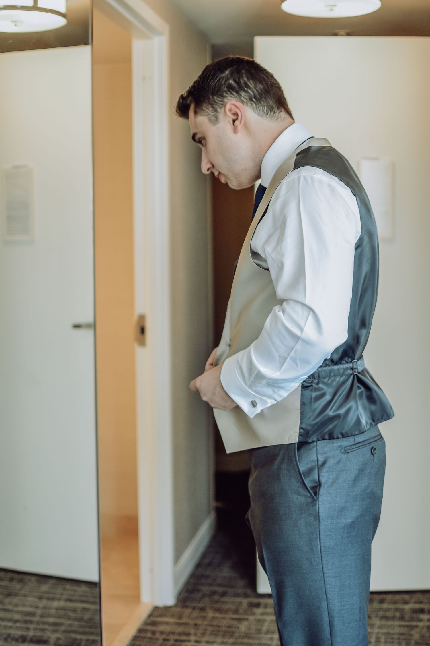 Multiple views of someone in a white shirt and gray vest looking down while standing in a carpeted hallway.