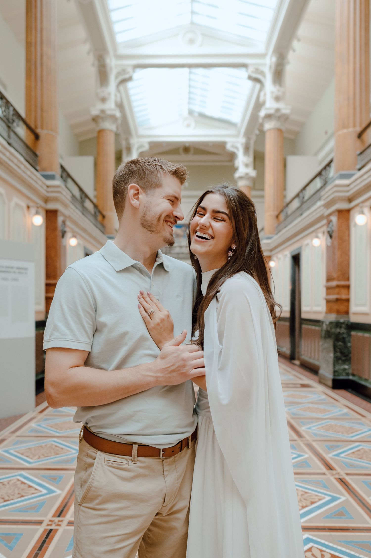 Couple sharing intimate moments in an ornate classical building hallway with patterned marble floors and elegant columns.