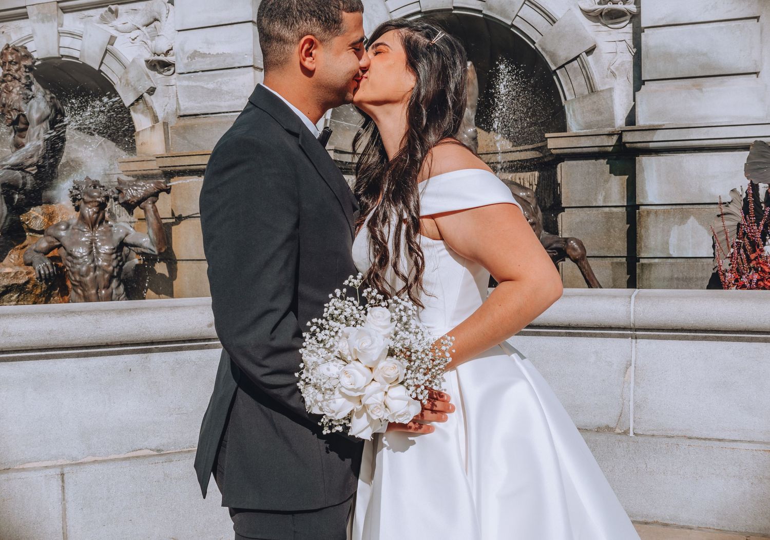 A romantic wedding kiss captured in front of classical architecture with white stone columns.