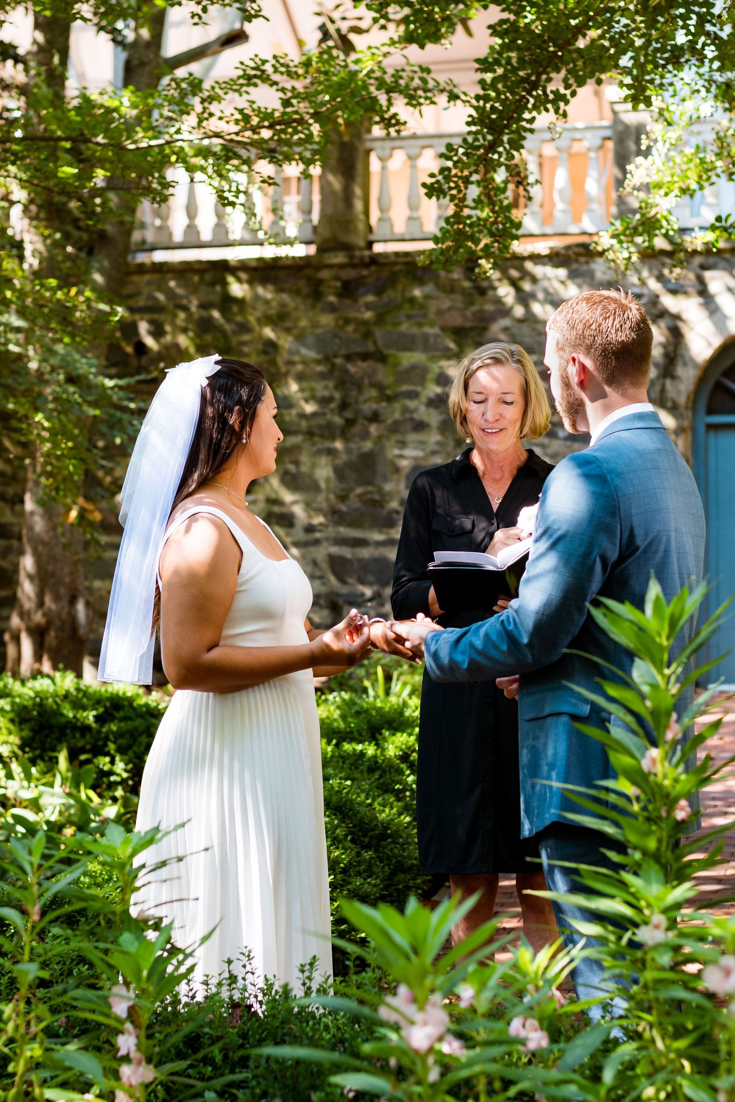 Outdoor wedding ceremony in lush garden setting with officiant and couple exchanging vows.