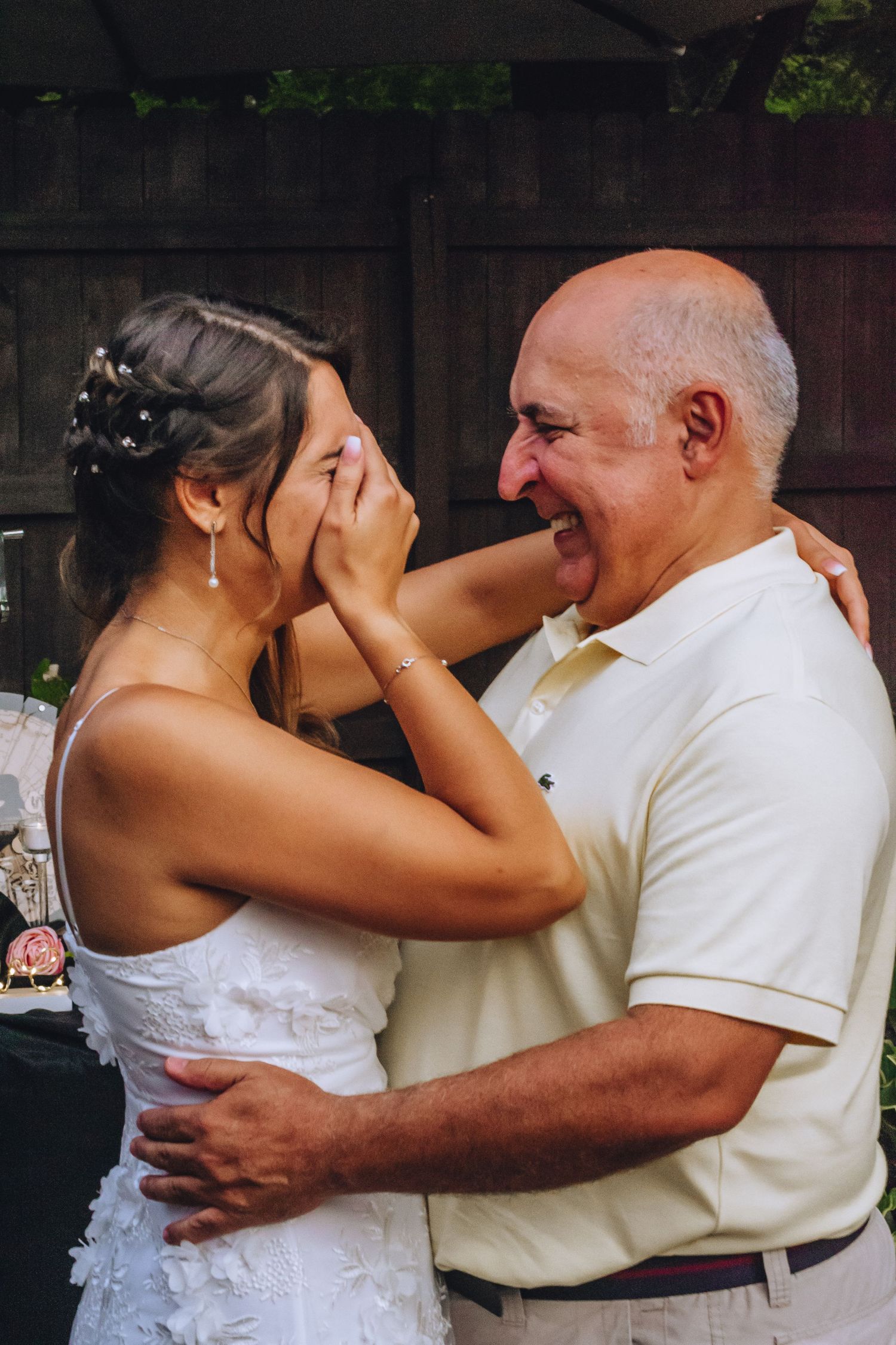 An emotional moment shared between a bride in a white dress and an older gentleman at an outdoor wedding celebration.