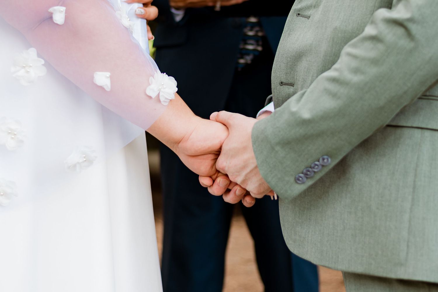 A person wearing a gray suit extends their right hand to someone wearing a white garment during a formal event.