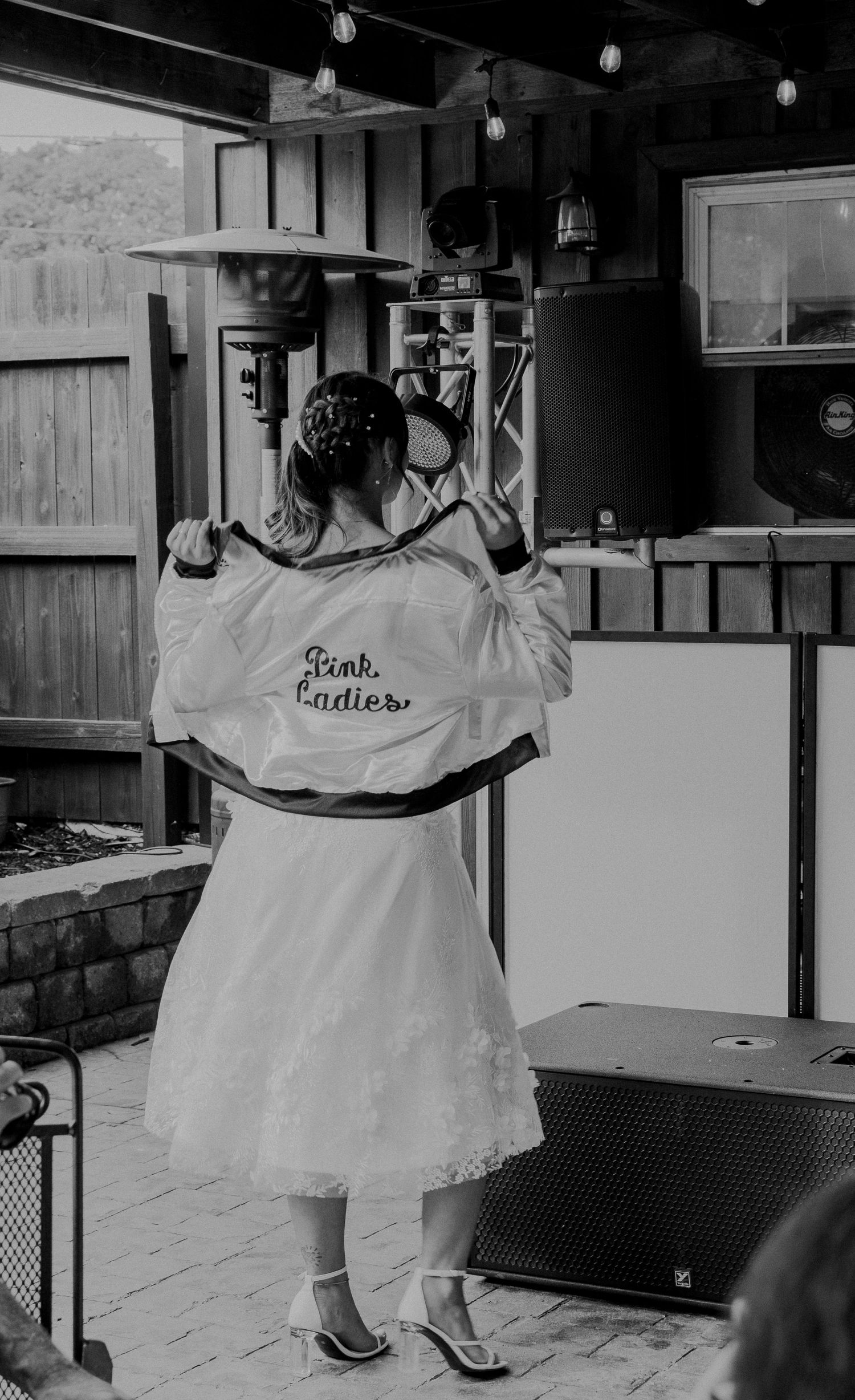 A person wearing a white dress and jacket with 'Best Brother' text stands at a venue in black and white photography.