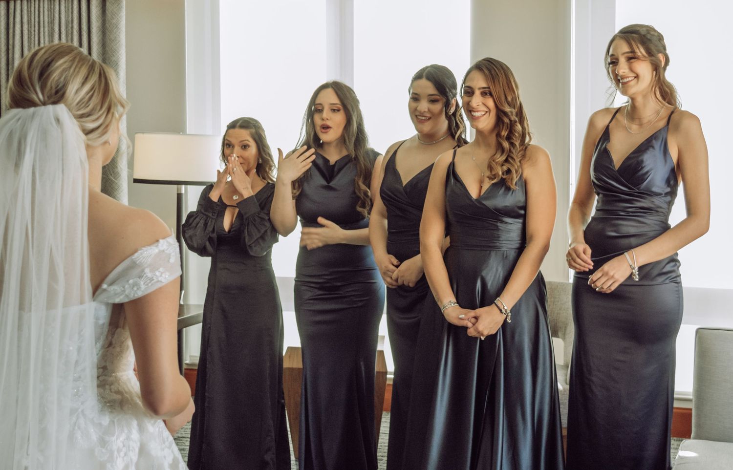 Bridesmaids in elegant navy blue dresses admire the bride in her white gown during an emotional first look moment.