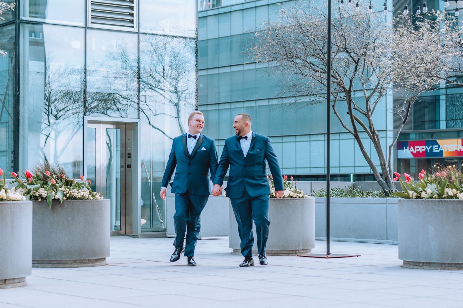 Business people walking through a modern office building lobby with glass walls and decorative planters.