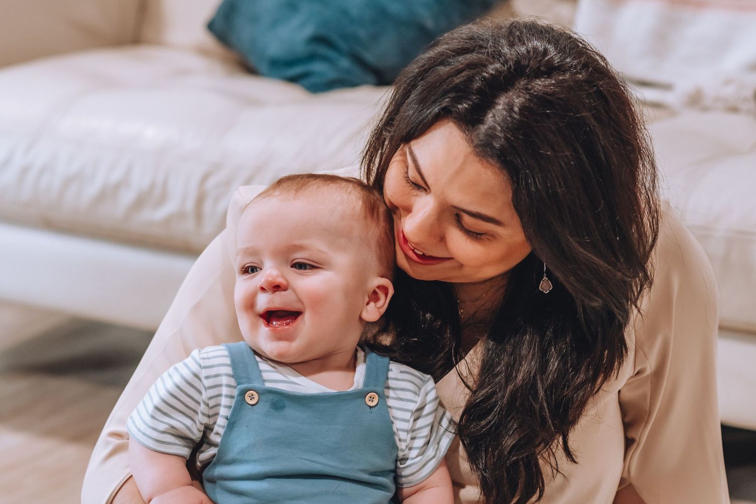 A playful moment shared between a parent and laughing baby wearing striped clothing on a couch.
