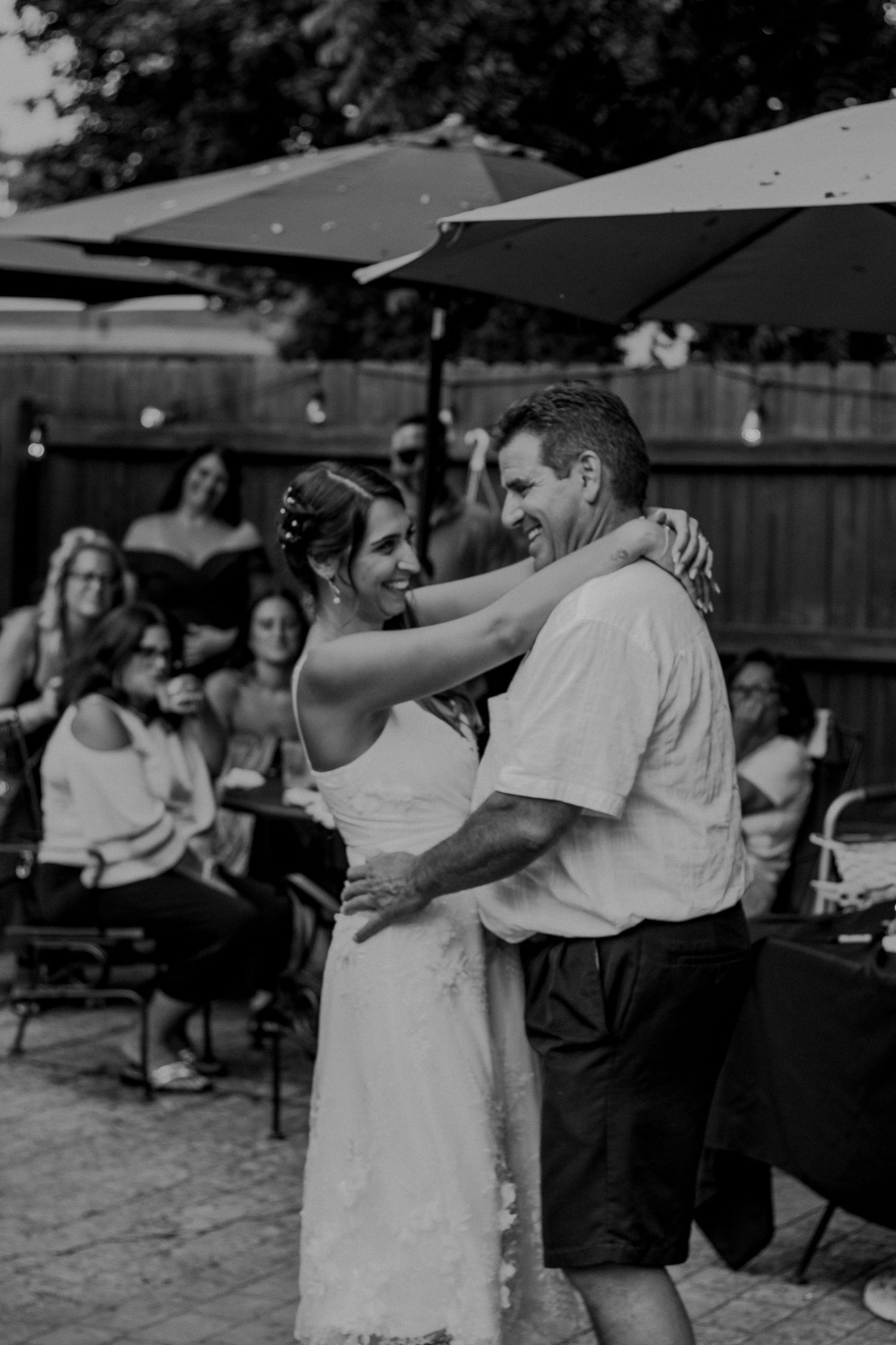 A tender black and white moment captured during a dance at an outdoor reception under patio umbrellas.