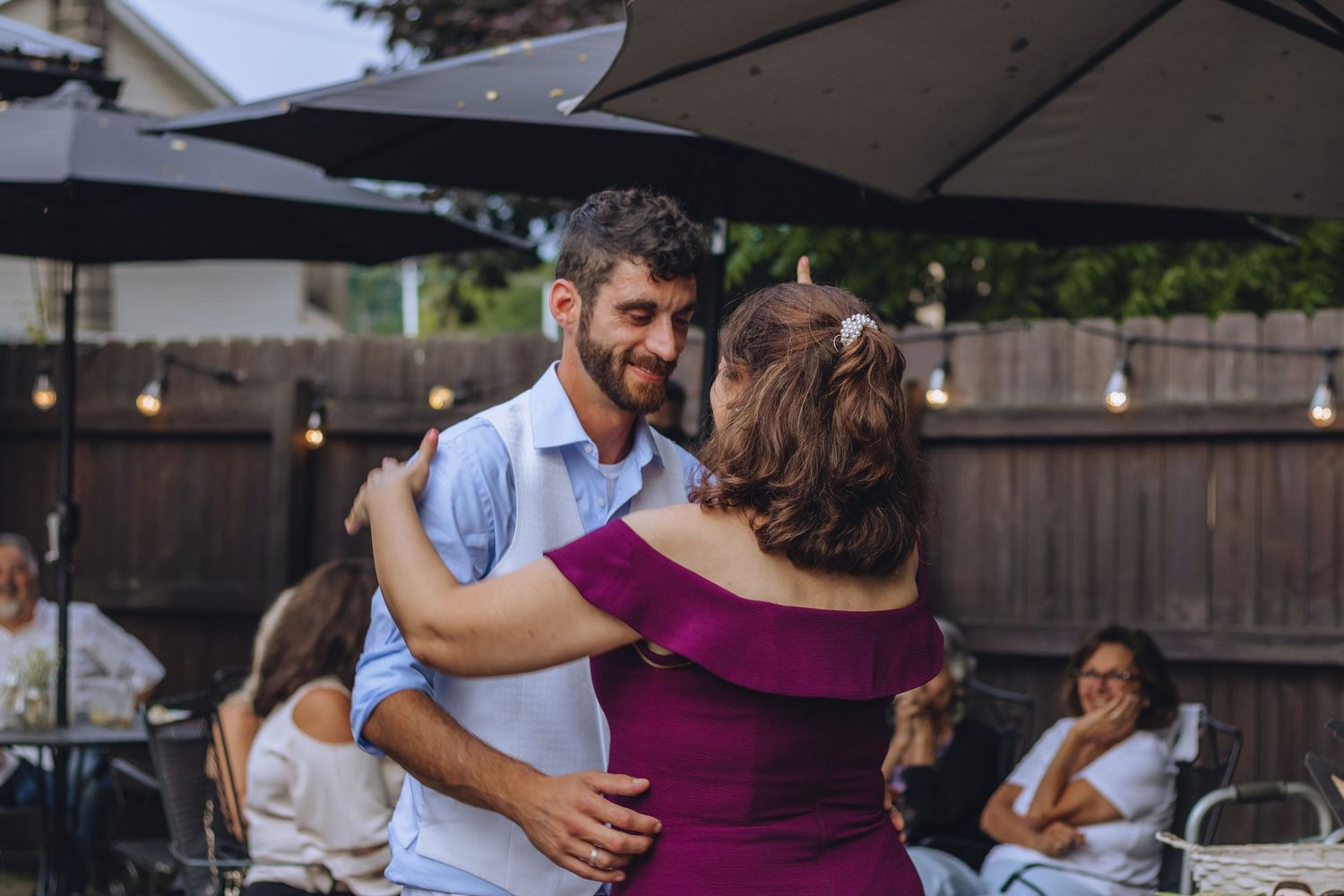 A couple dancing outdoors under a covered patio area with trees and fencing in the background.