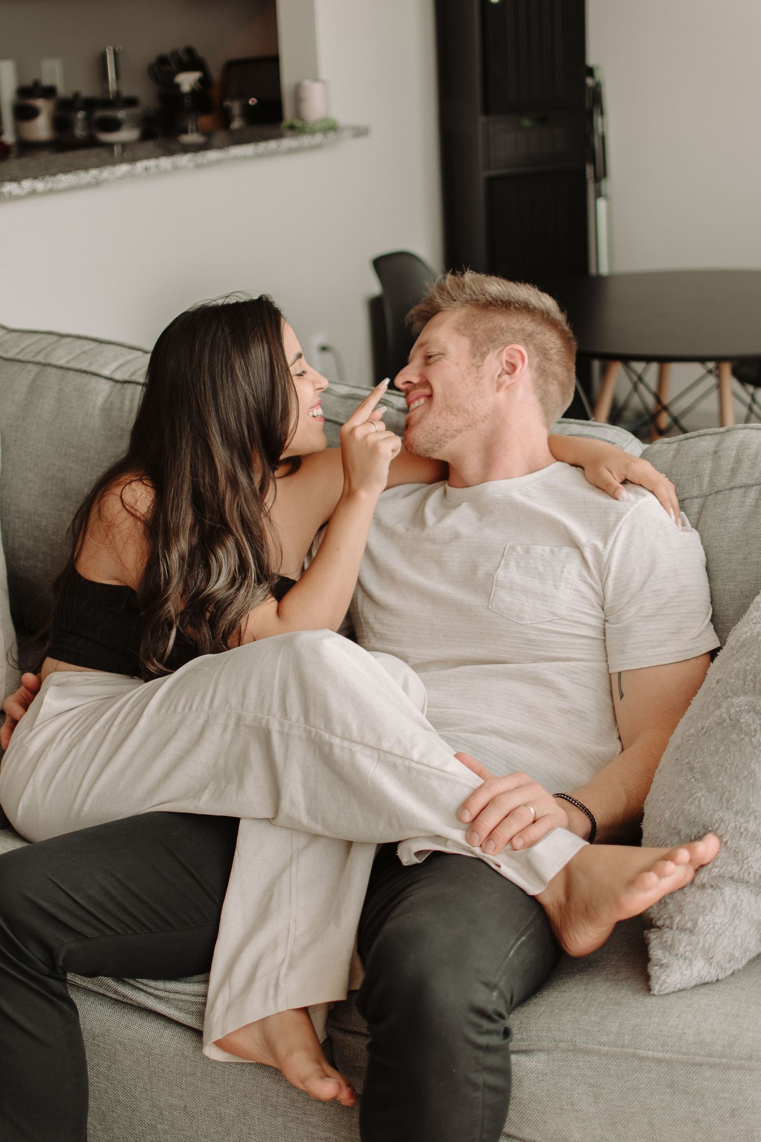 Couple sharing an intimate playful moment while relaxing together on a cozy grey couch at home.