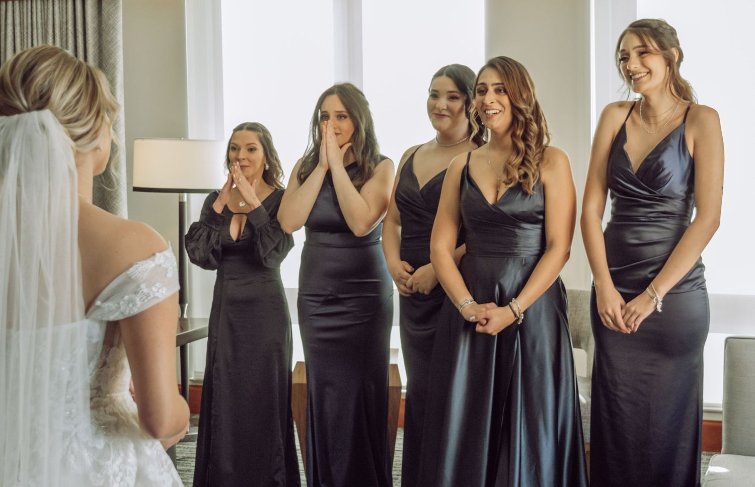 A group in navy bridesmaid dresses share an emotional first look moment with the bride in a white gown.