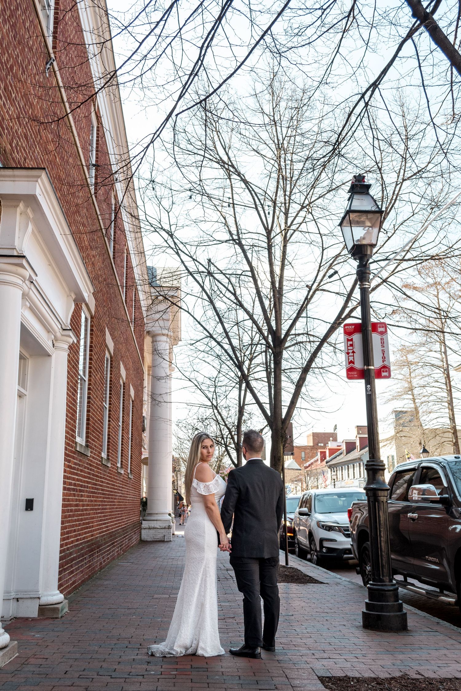 Romantic wedding photo on brick sidewalk with vintage lamp post and historic architecture.