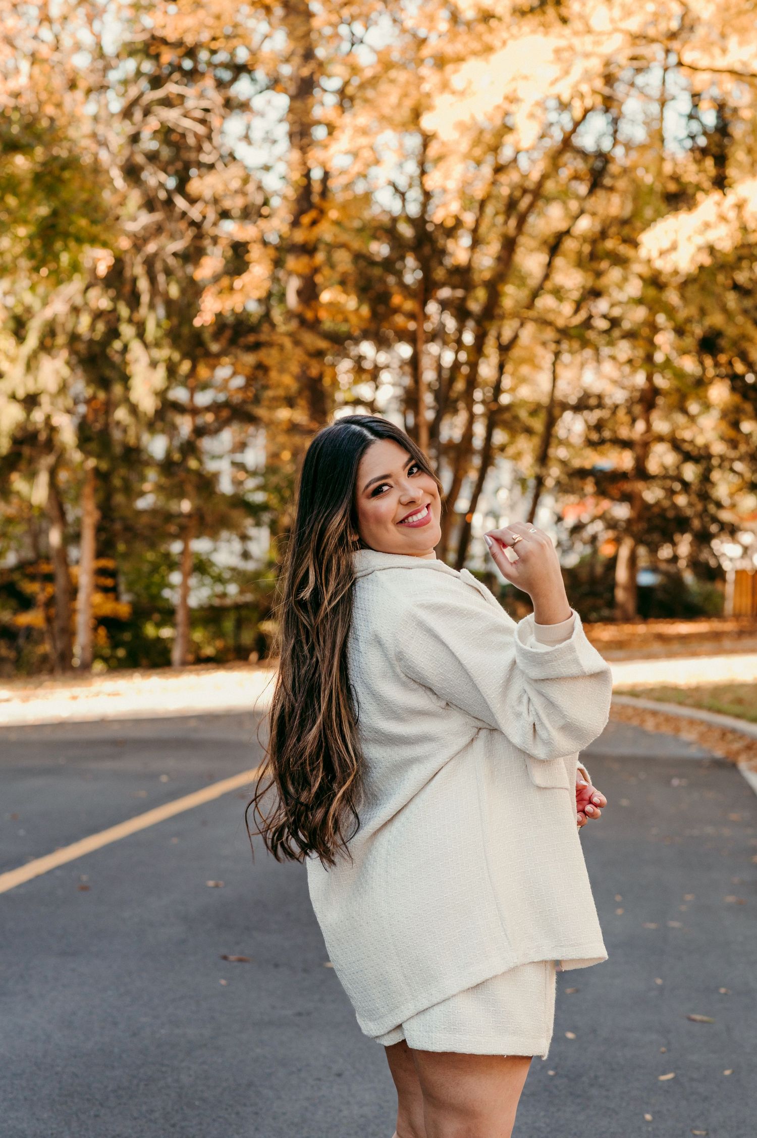Candid autumn outdoor portrait showing a person in a cozy white sweater turning back on a tree-lined road.