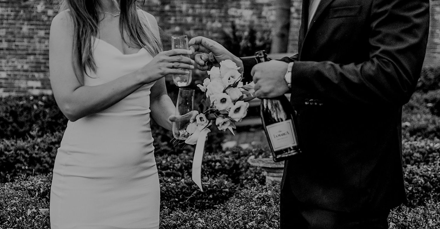 A couple pours wine into glasses during an intimate black and white outdoor ceremony moment.