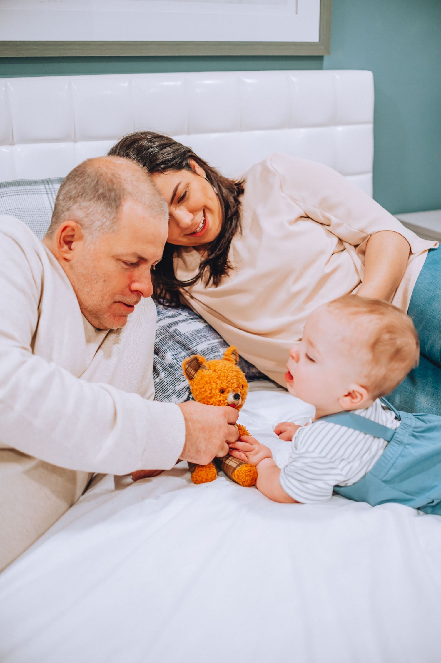 Family cuddles together on bed with baby's orange plush toy.