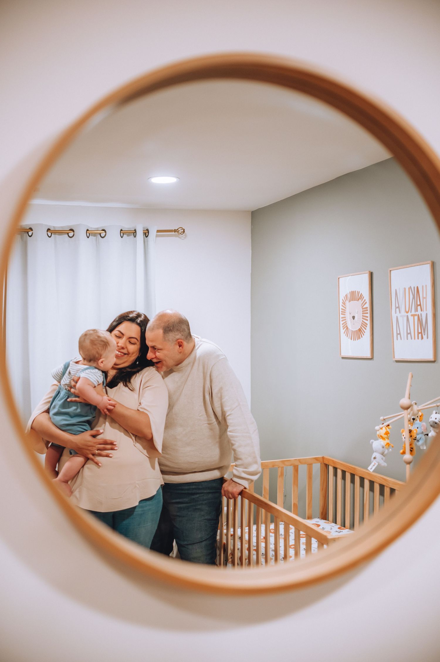 Mirror reflection captures a sweet family moment in a decorated nursery with mobile and artwork.