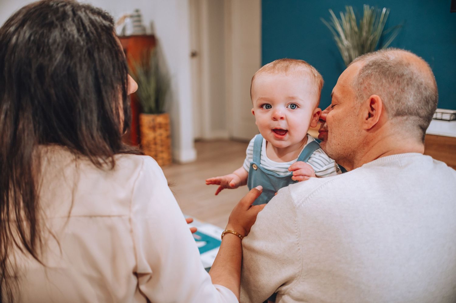 Happy baby in blue outfit shares joyful moment with adults during playtime.