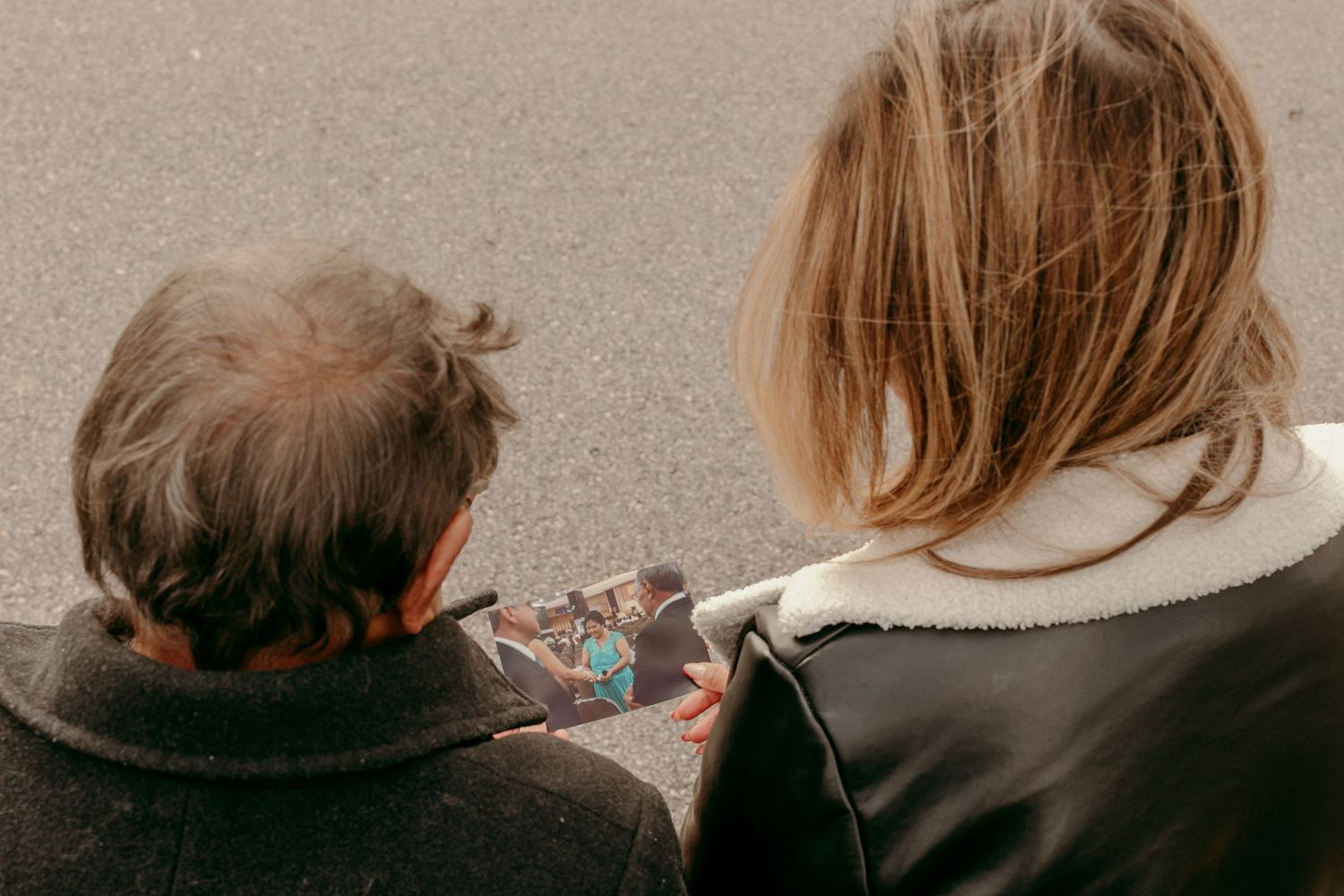 Two people in dark coats looking down at something together while sitting outdoors.