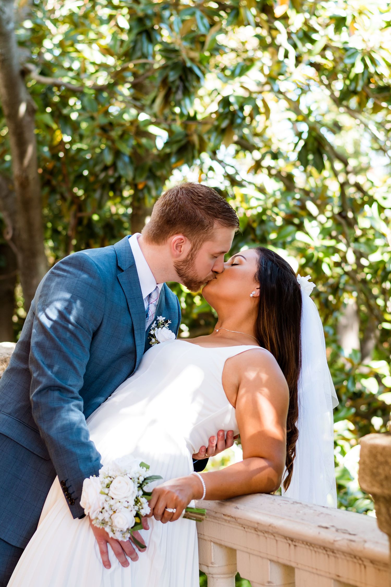 Romantic outdoor wedding portrait with couple sharing a tender moment by stone railing.