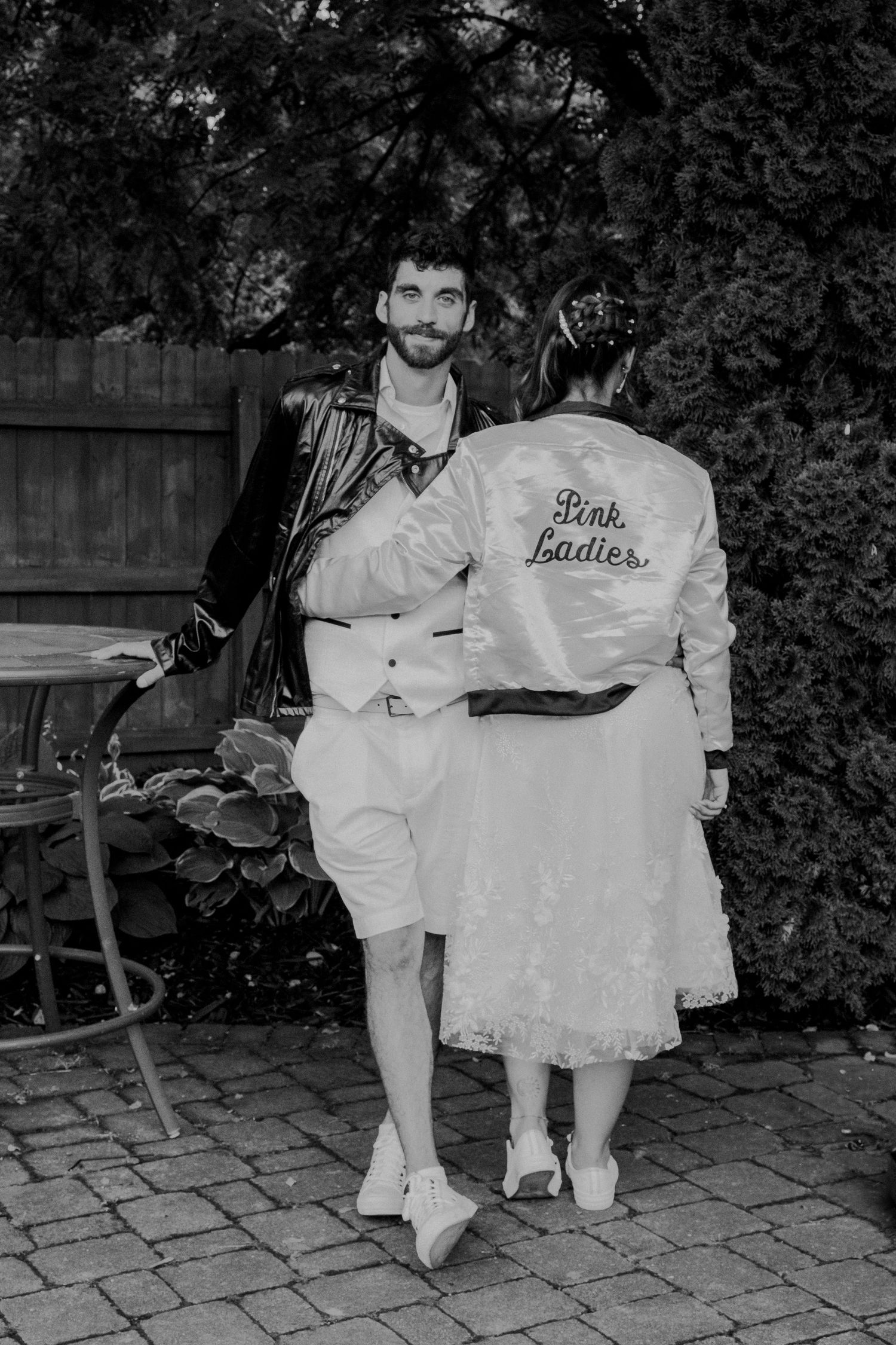 Black and white photo of a couple in contrasting outfits - one in black leather jacket, the other in a white satin jacket.