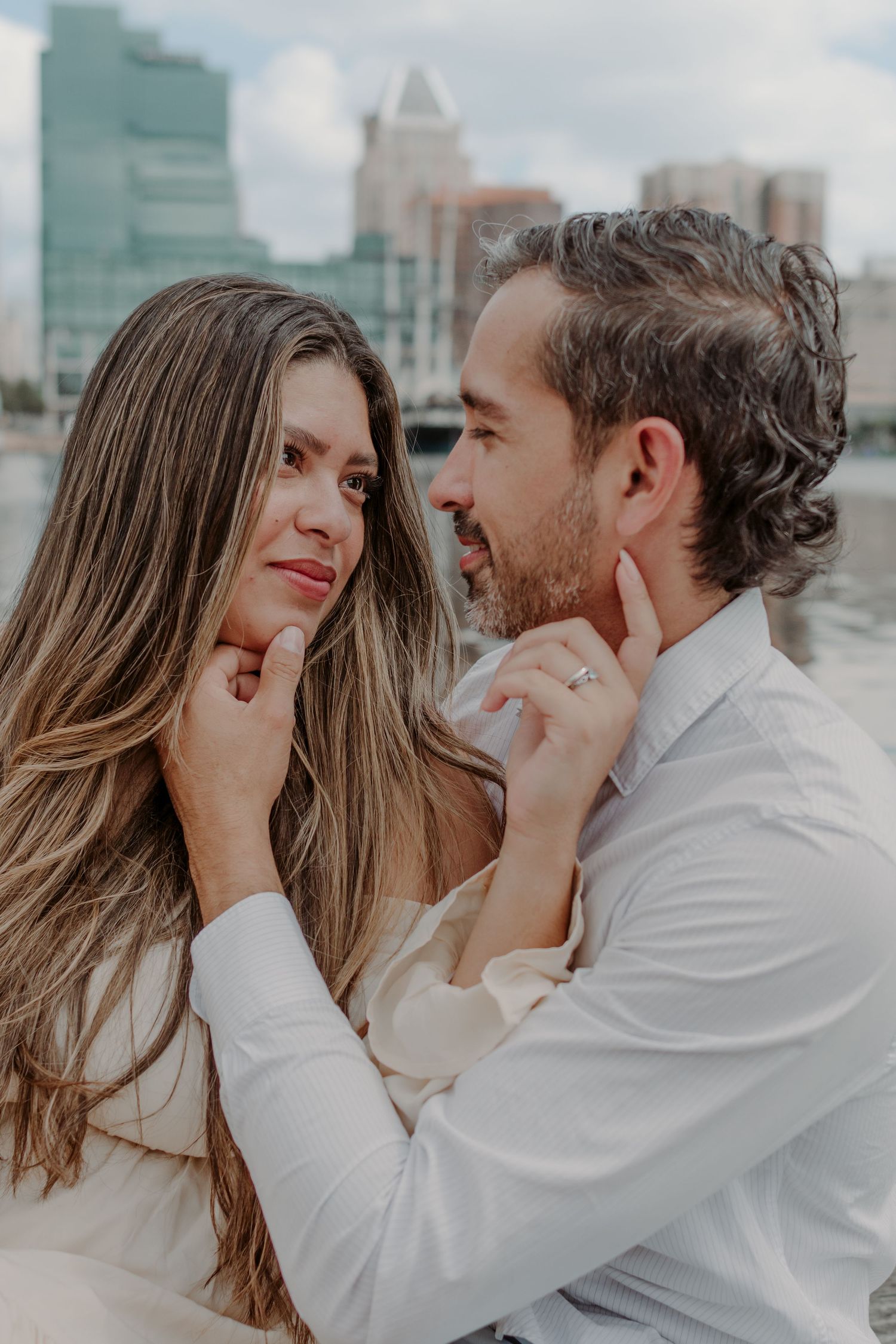 Romantic couple sharing an intimate moment while wearing white outfits against a city backdrop.