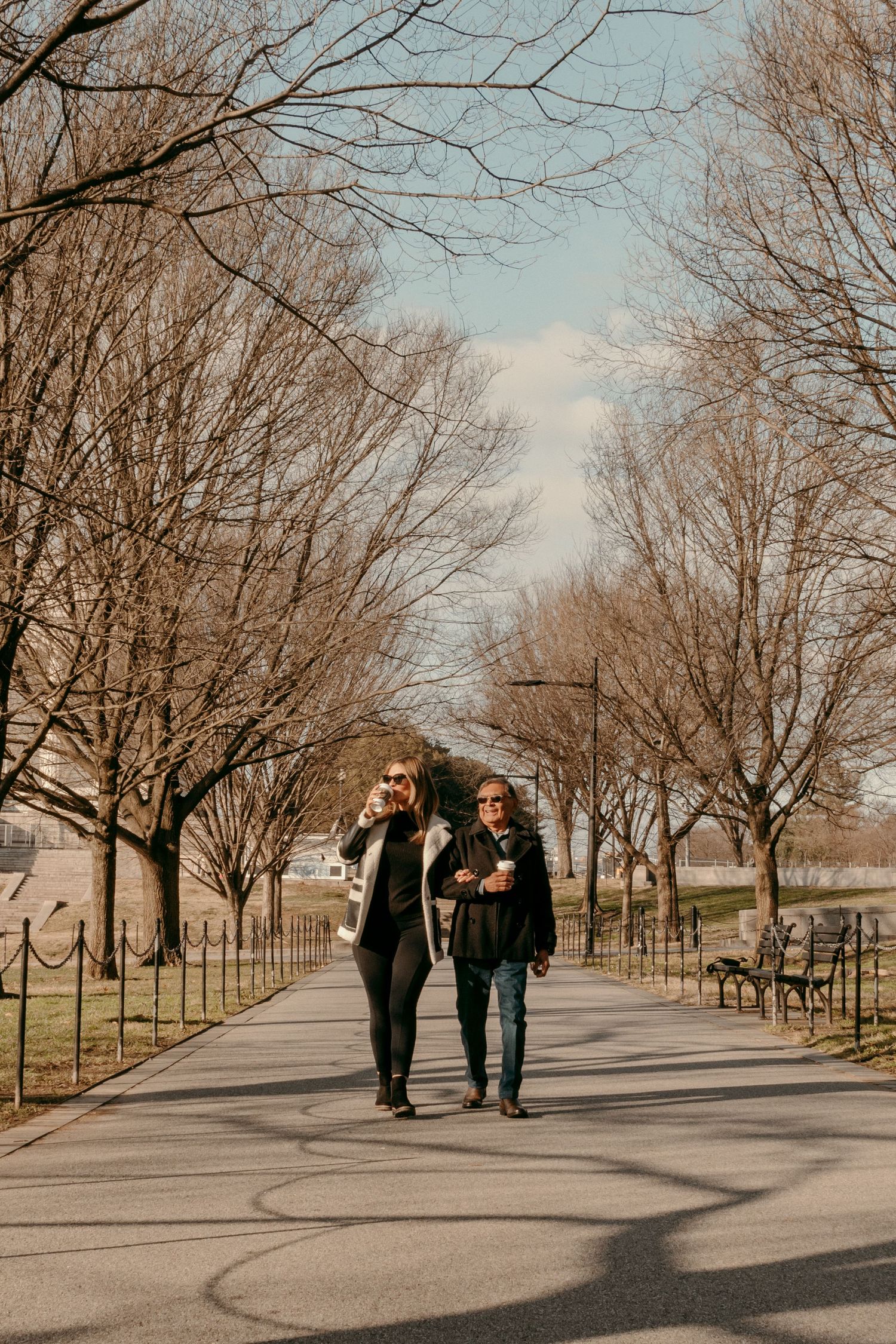 Two people walking together along a tree-lined path in a park during fall.