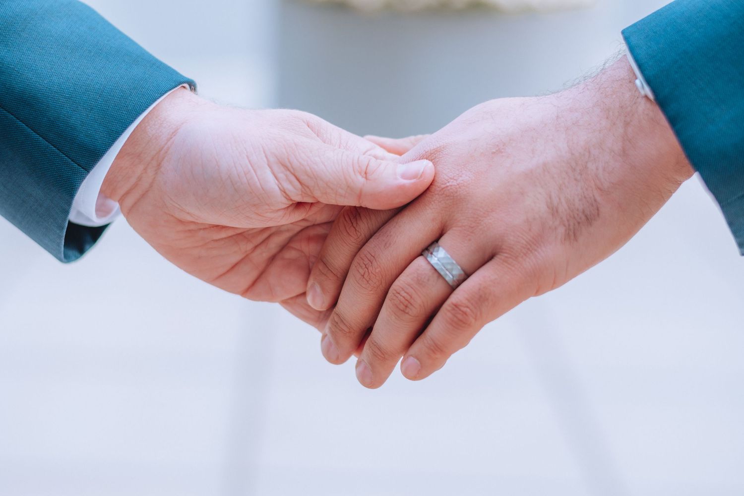 Close-up view of two hands gently holding each other against a soft white background.