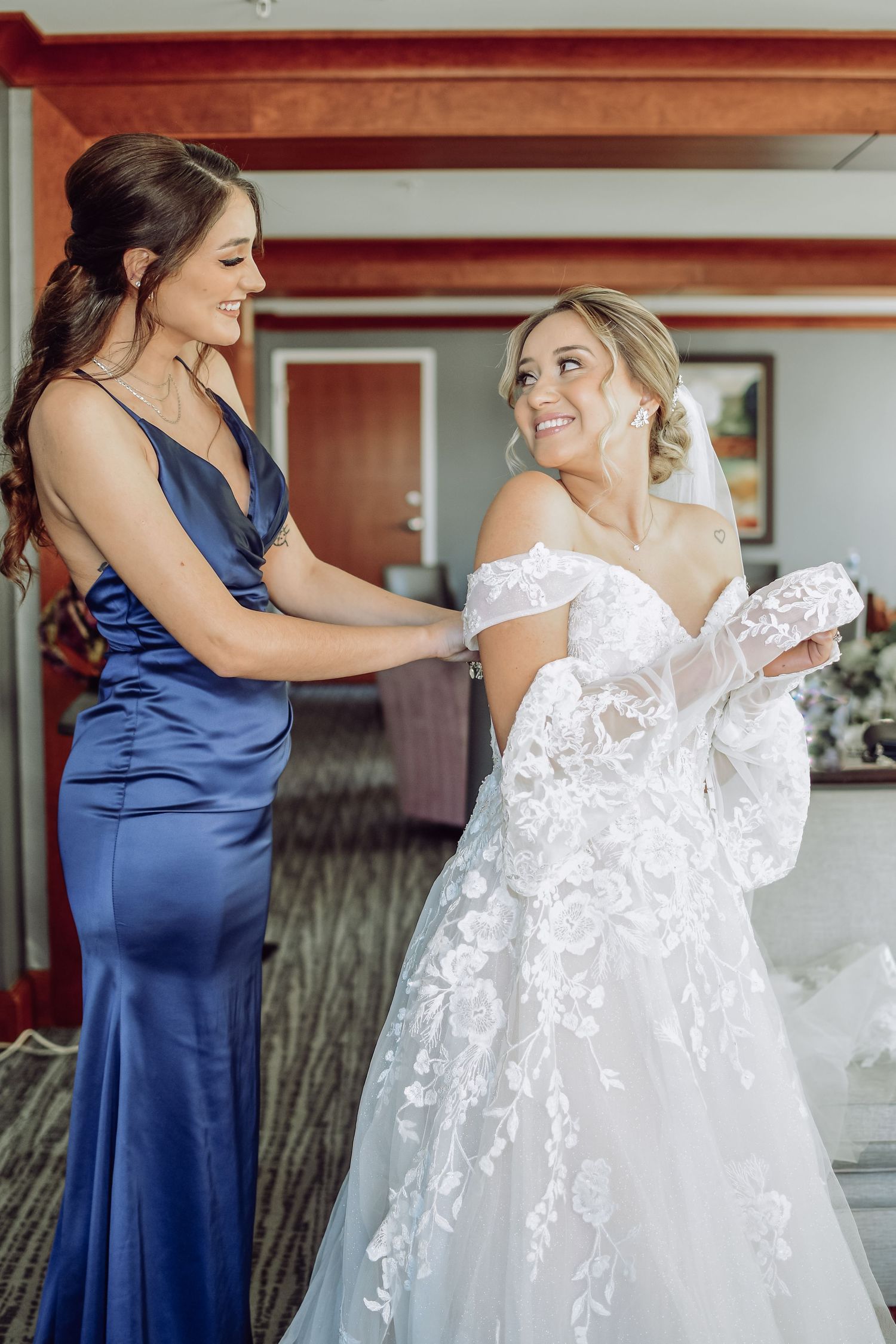A series of images showing a bride in a white lace gown being helped into her dress by an attendant in navy blue.