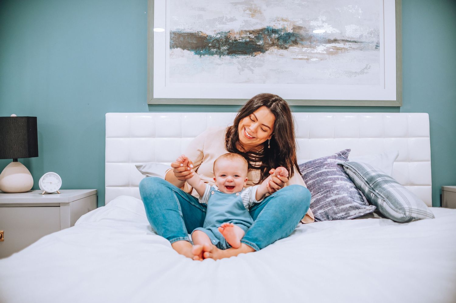A joyful moment between parent and baby relaxing together on a white bed with teal wall decor.