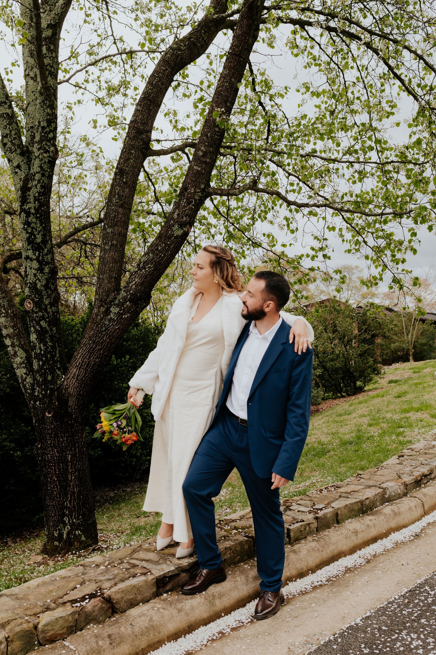 A couple in wedding attire share a romantic moment against a tree-lined path on their special day.