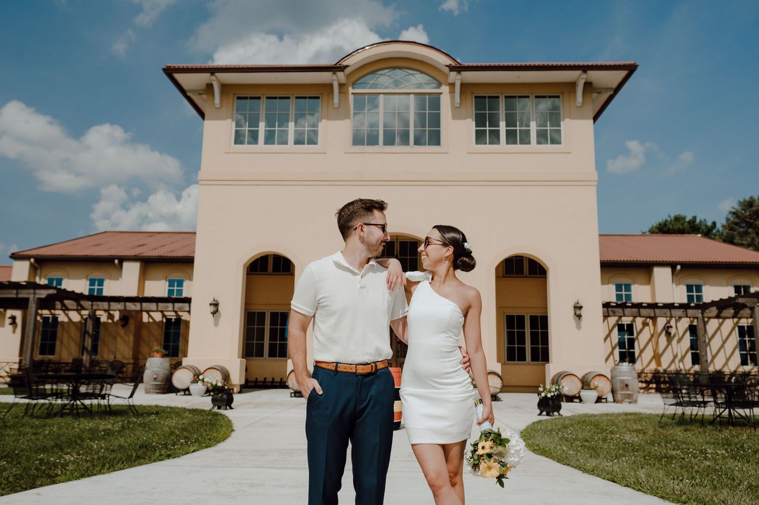 A couple shares a joyful moment together outside a Mediterranean-style villa with cream stucco walls and arched doorways.