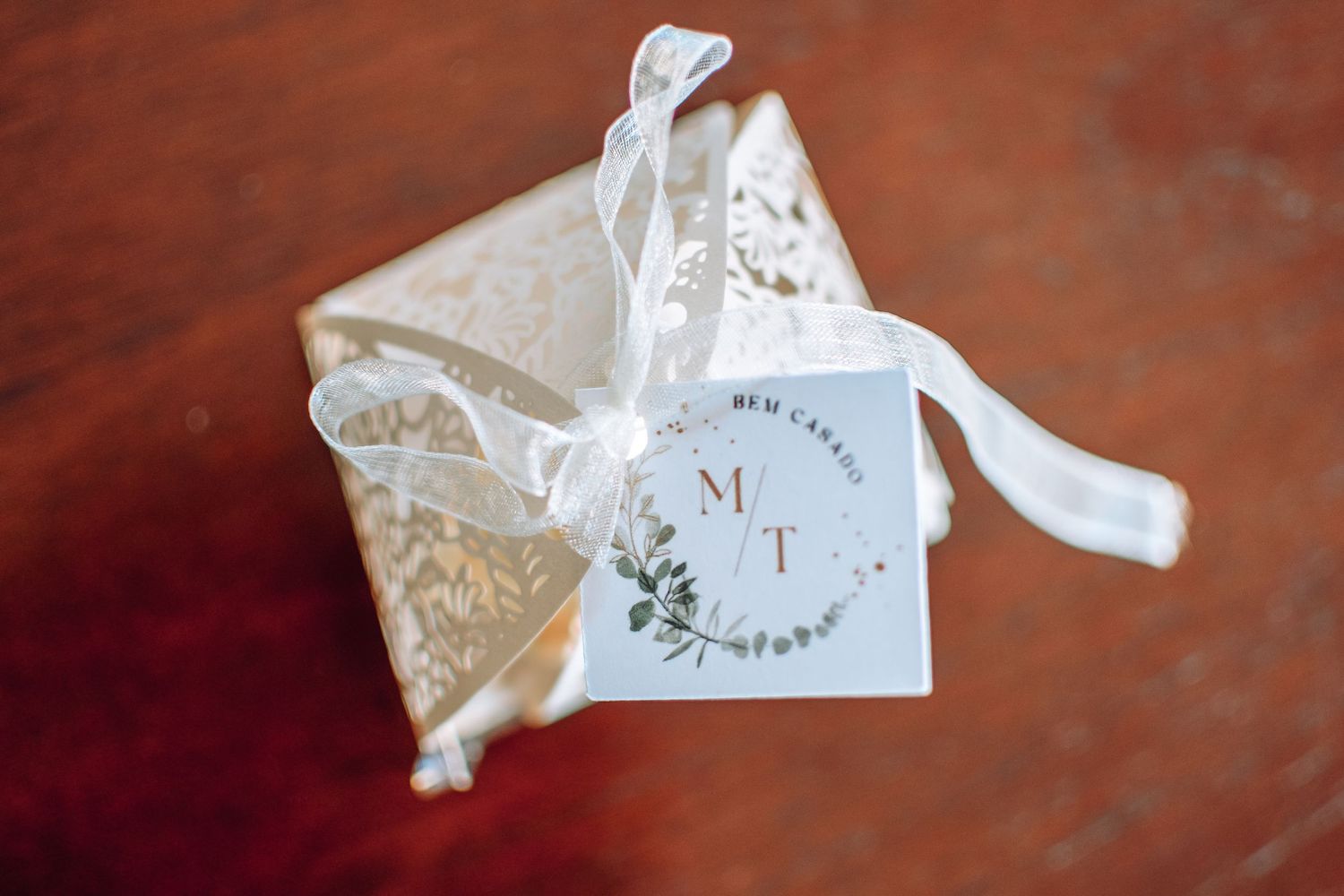 White wedding favor box with delicate lace pattern and tag tied with ribbon on brown wooden surface.