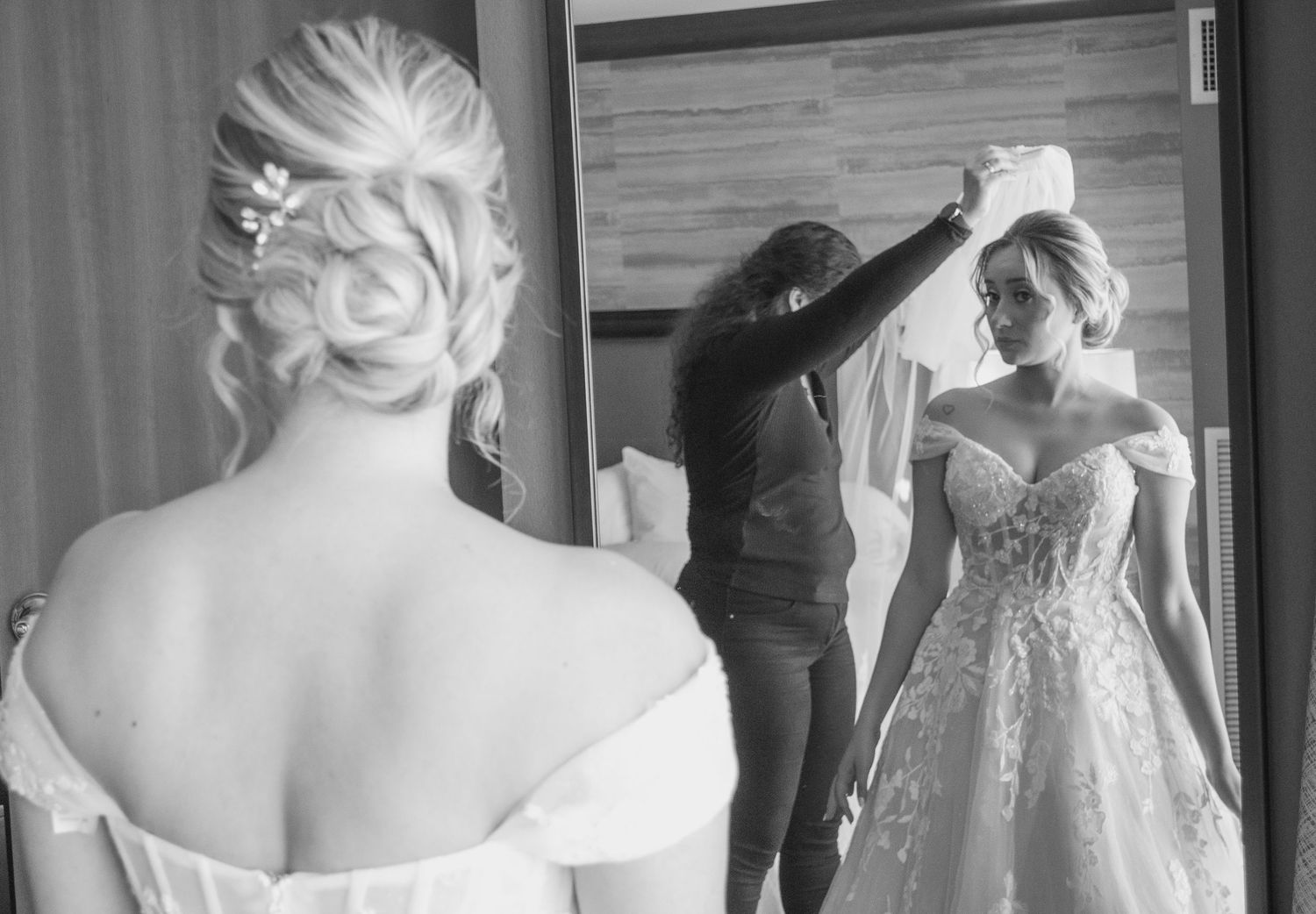 A candid black and white photo showing final preparations of a bride getting ready in her detailed lace wedding gown.