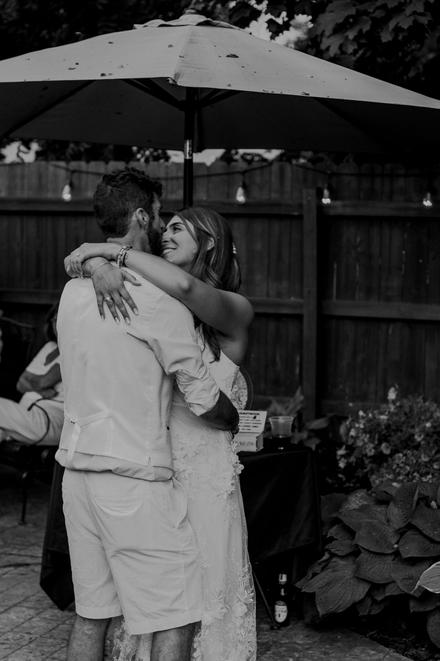 A romantic black and white dance moment in a backyard garden setting under a patio umbrella.