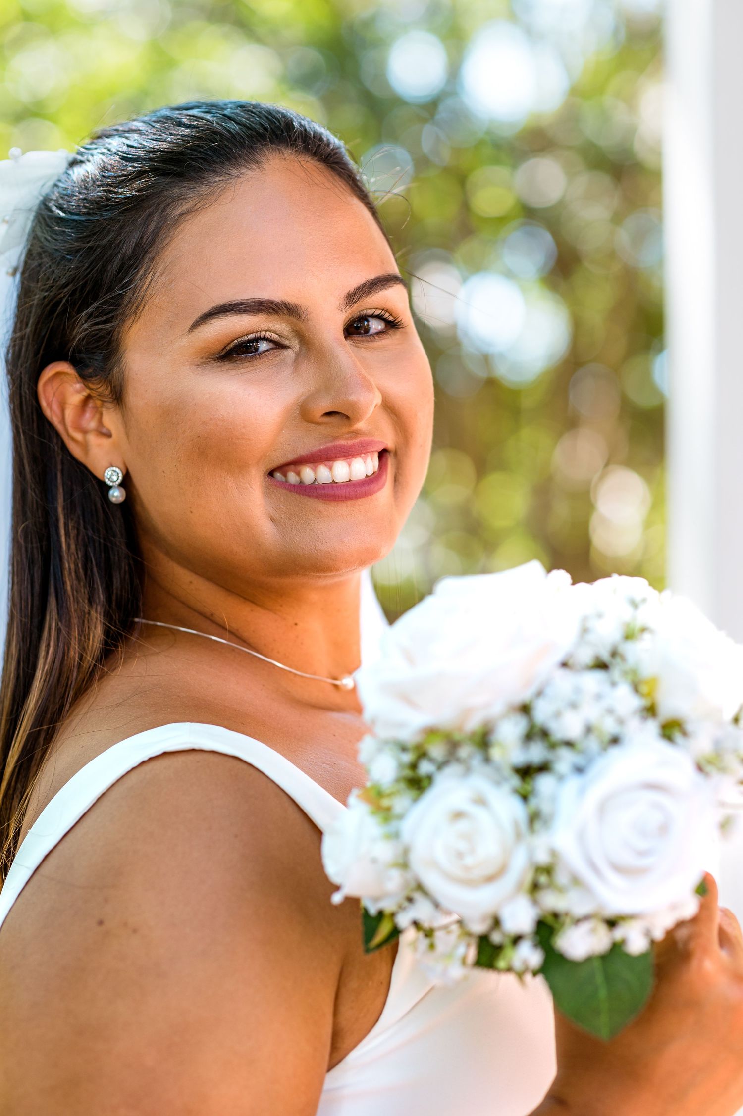 Radiant bride holding white rose bouquet poses in outdoor wedding setting.