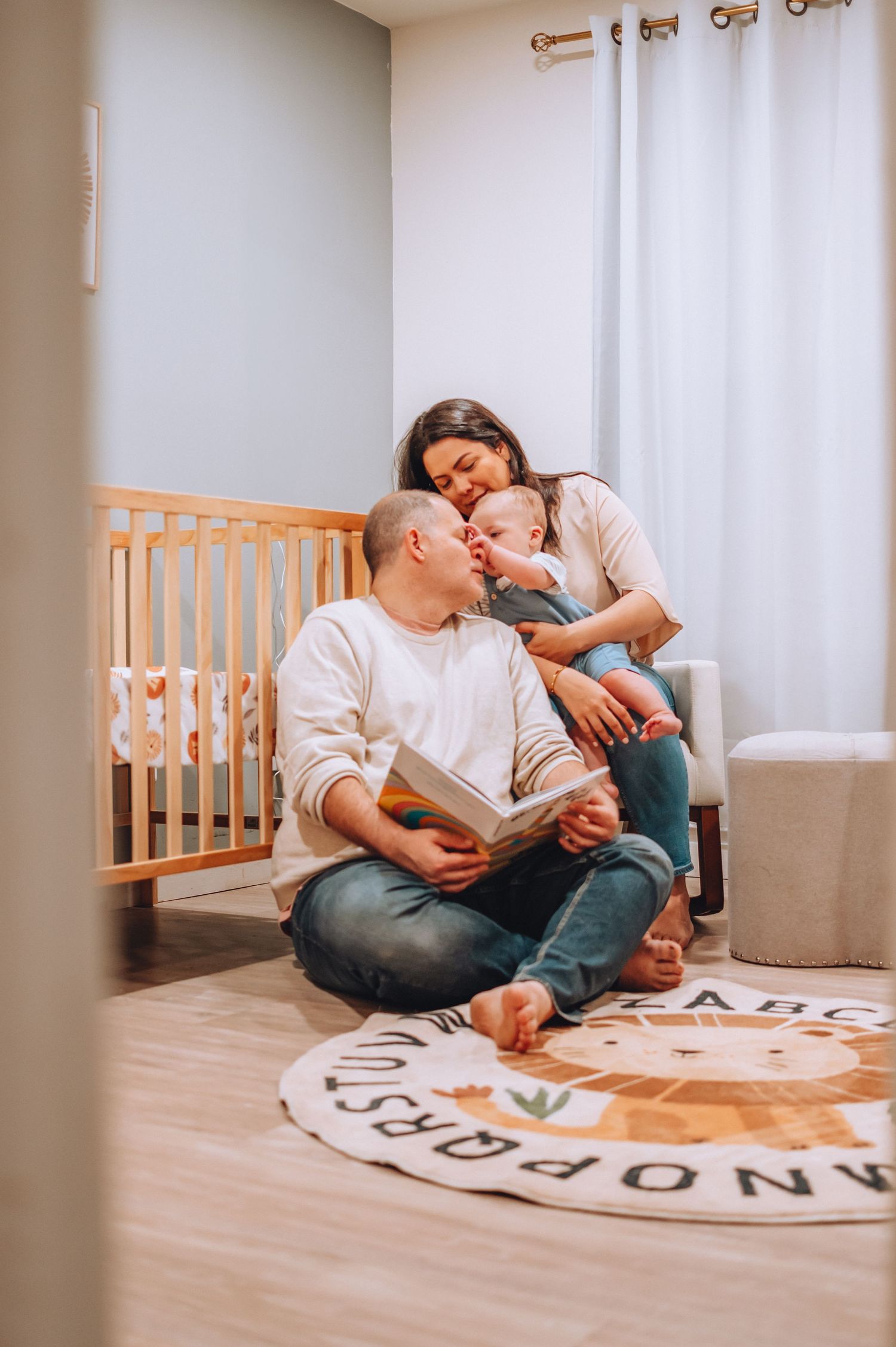 A heartwarming family moment in a nursery as they read together on a decorative round rug near a wooden crib.