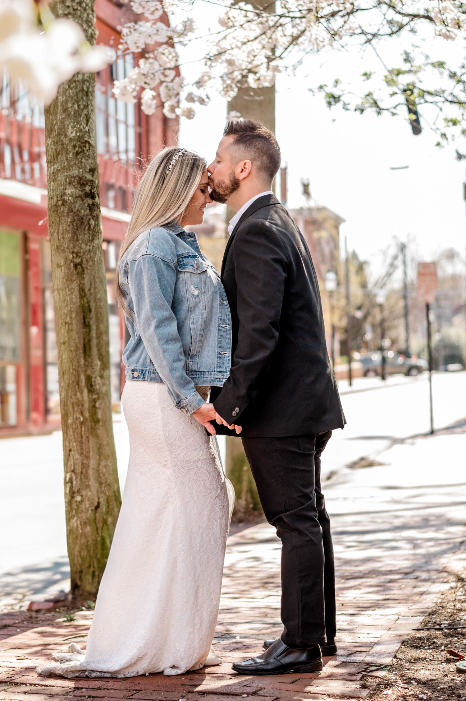 Intimate wedding moment captured under spring cherry blossoms on urban street.
