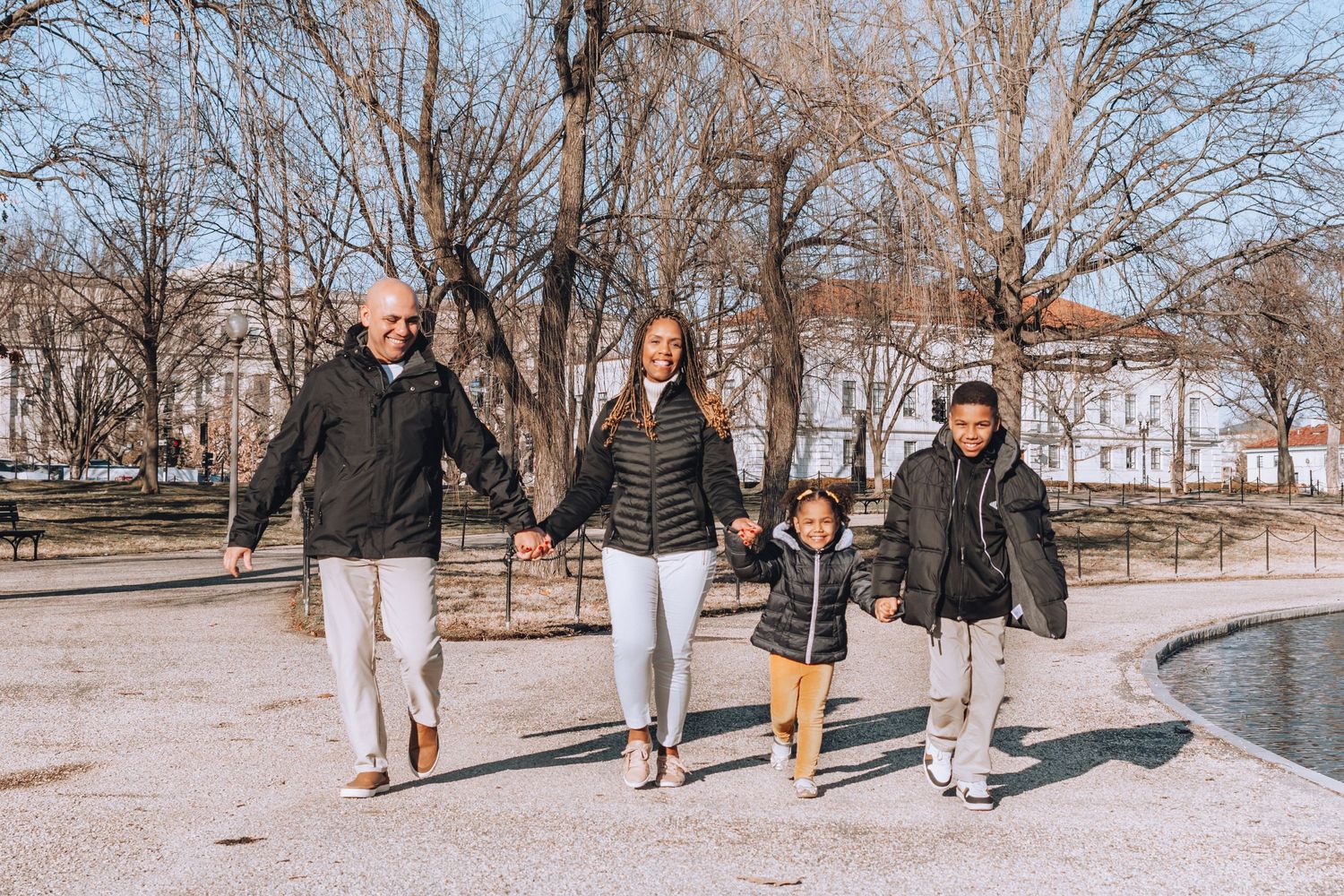 Family holding hands while walking along path near water with Washington Monument visible.