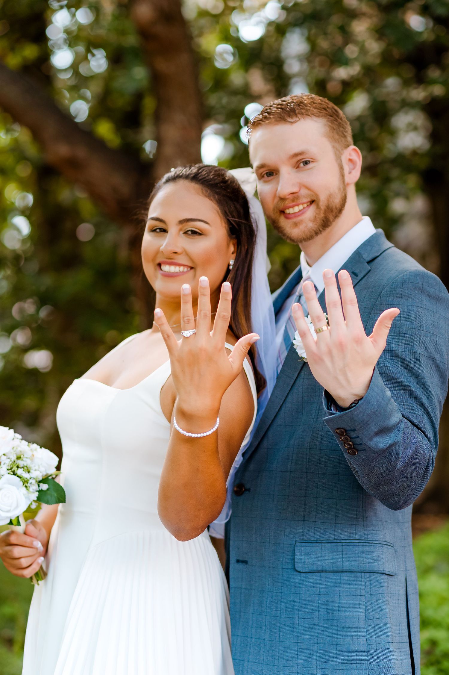 Joyful couple displaying their wedding rings while smiling in outdoor setting with natural lighting.