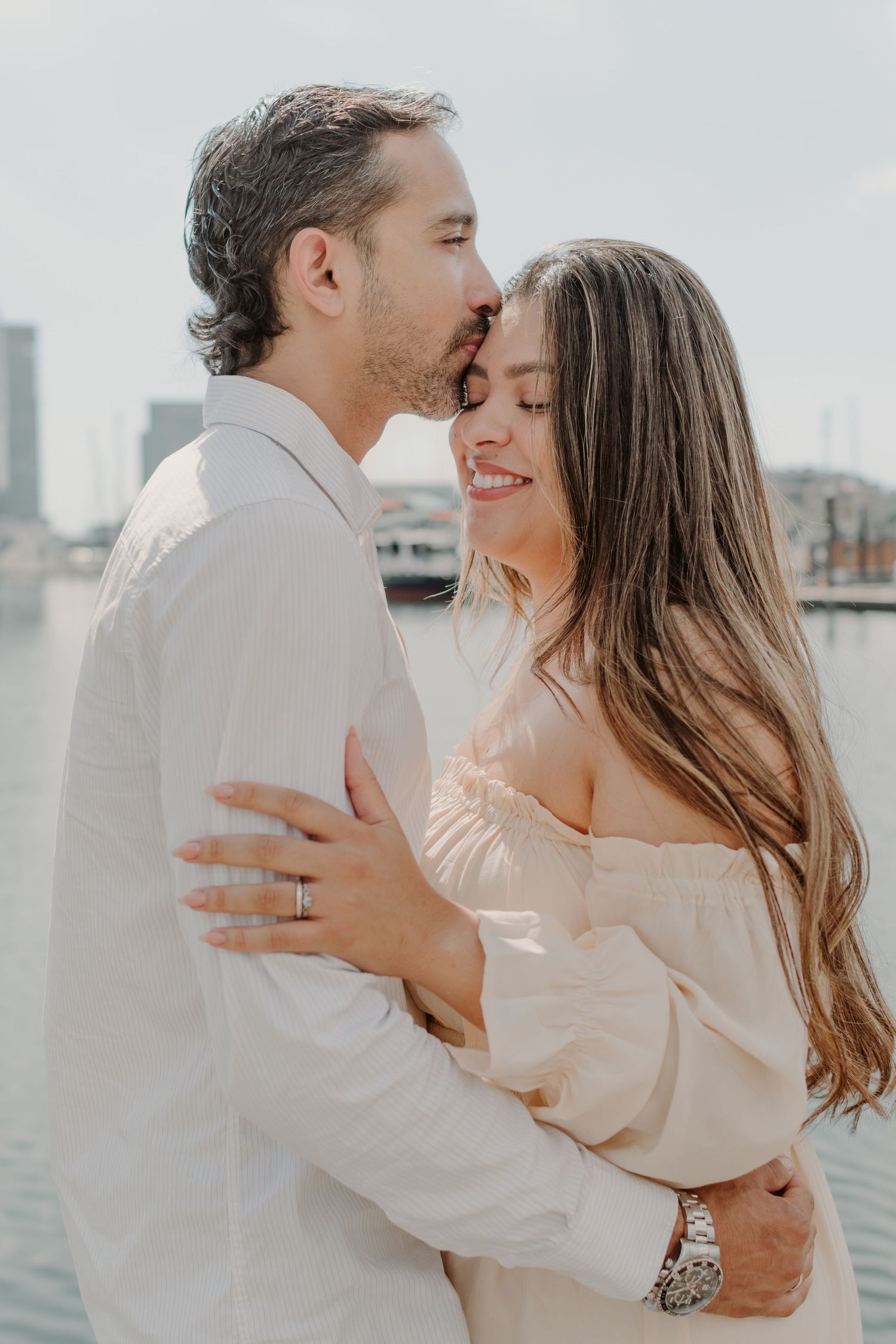A tender moment between a couple in white clothing against a bright urban backdrop.