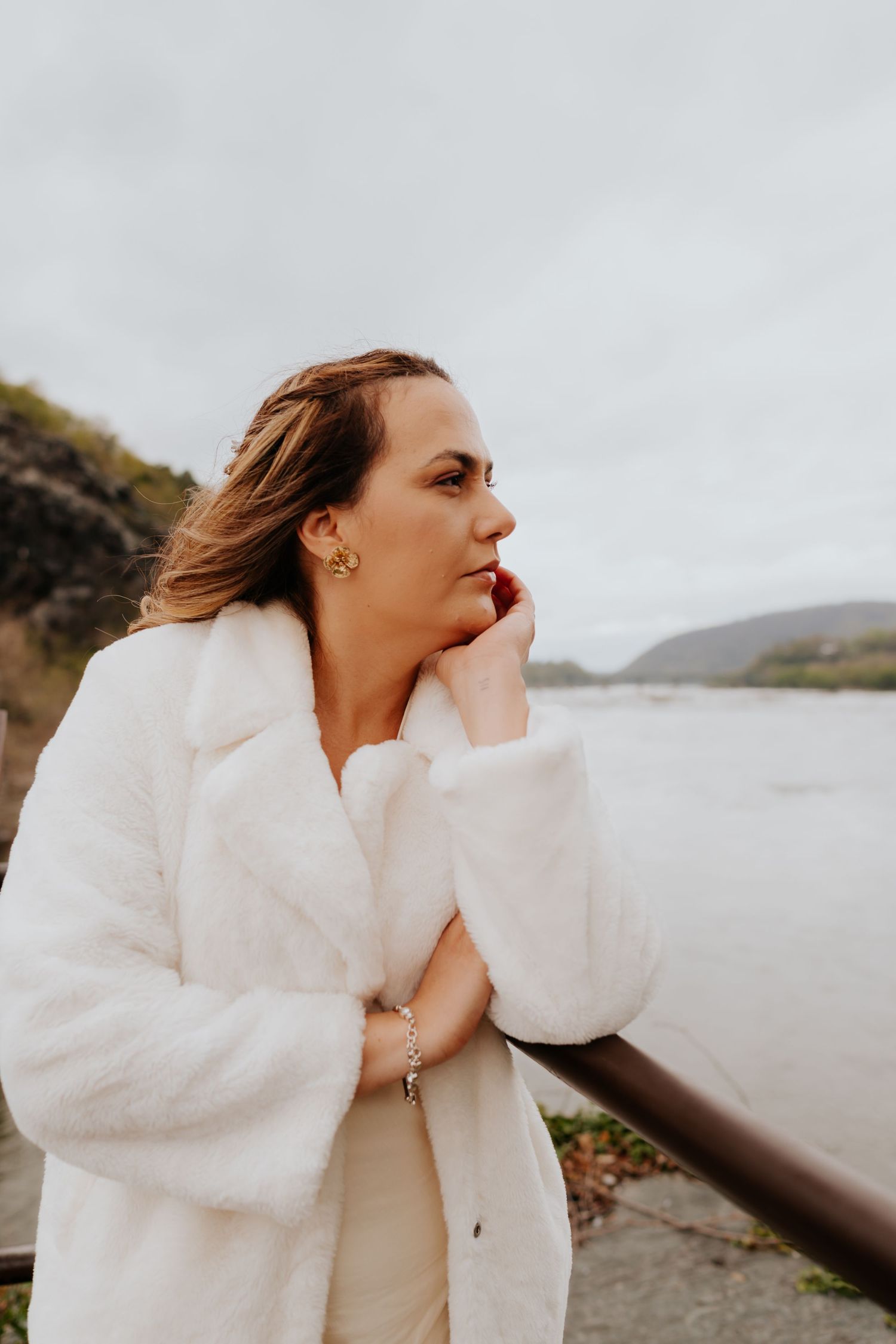 A contemplative woman in a white winter coat gazes at a scenic waterfront view.