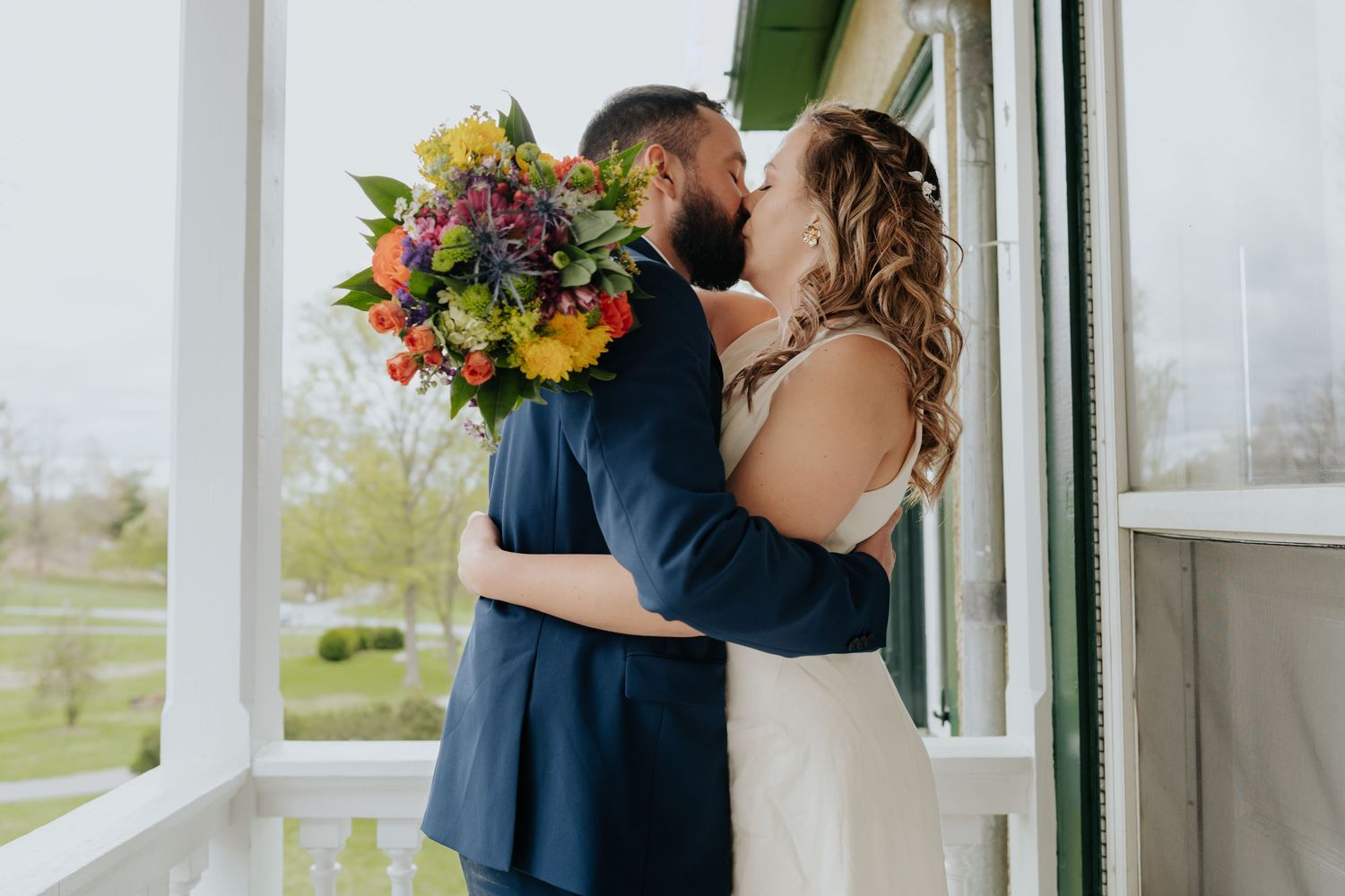 A couple shares a romantic moment together on a porch while the bride holds a vibrant autumn bouquet.