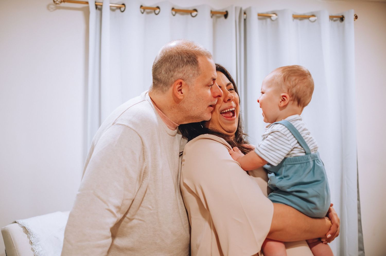Candid family moment showing affection and laughter in a bright nursery setting.