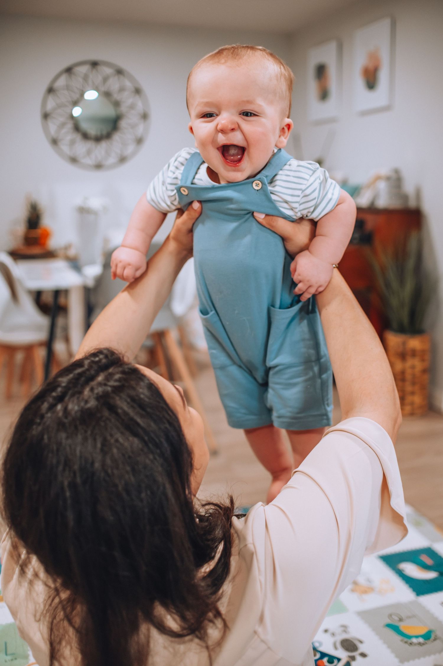 Baby in blue overalls laughs with delight while being lifted in the air.
