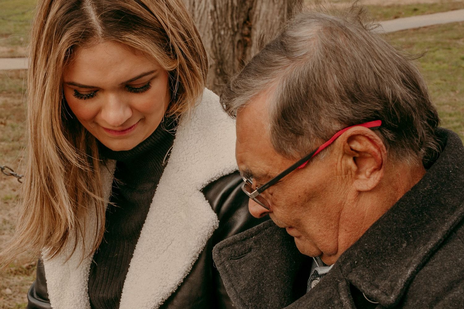 Two people sitting together outdoors while looking down at something.