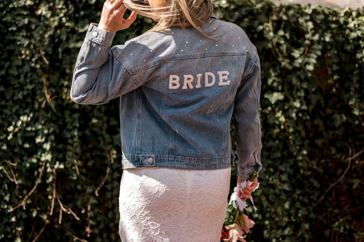 Denim jacket with 'BRIDE' text on the back styled with a white lace dress.