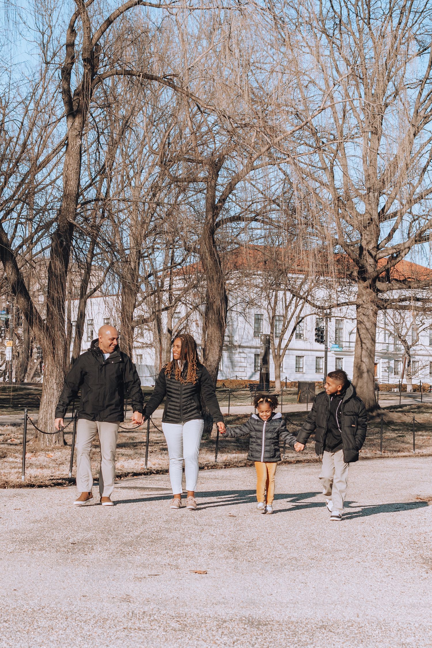 Family takes winter stroll along path with historic buildings visible through bare trees.
